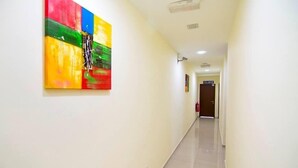 A hallway with a colorful abstract painting on the left wall, a fire extinguisher mounted on the wall, and a door at the end of the hallway. - Sg Pelek Hotel (Sungai Pelek)