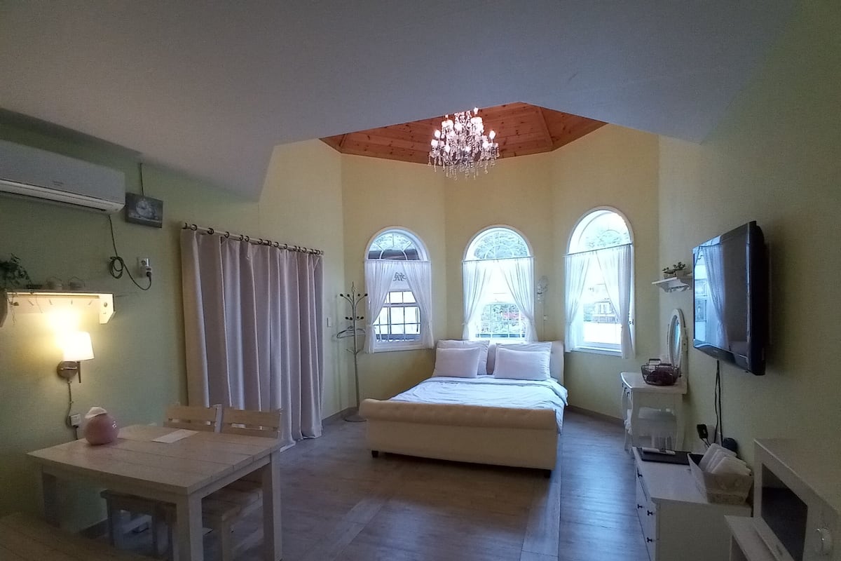 Un dormitorio con cama, escritorio, silla, televisor y candelabro.