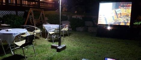Un patio al aire libre con mesas y sillas, un proyector y una computadora portátil.