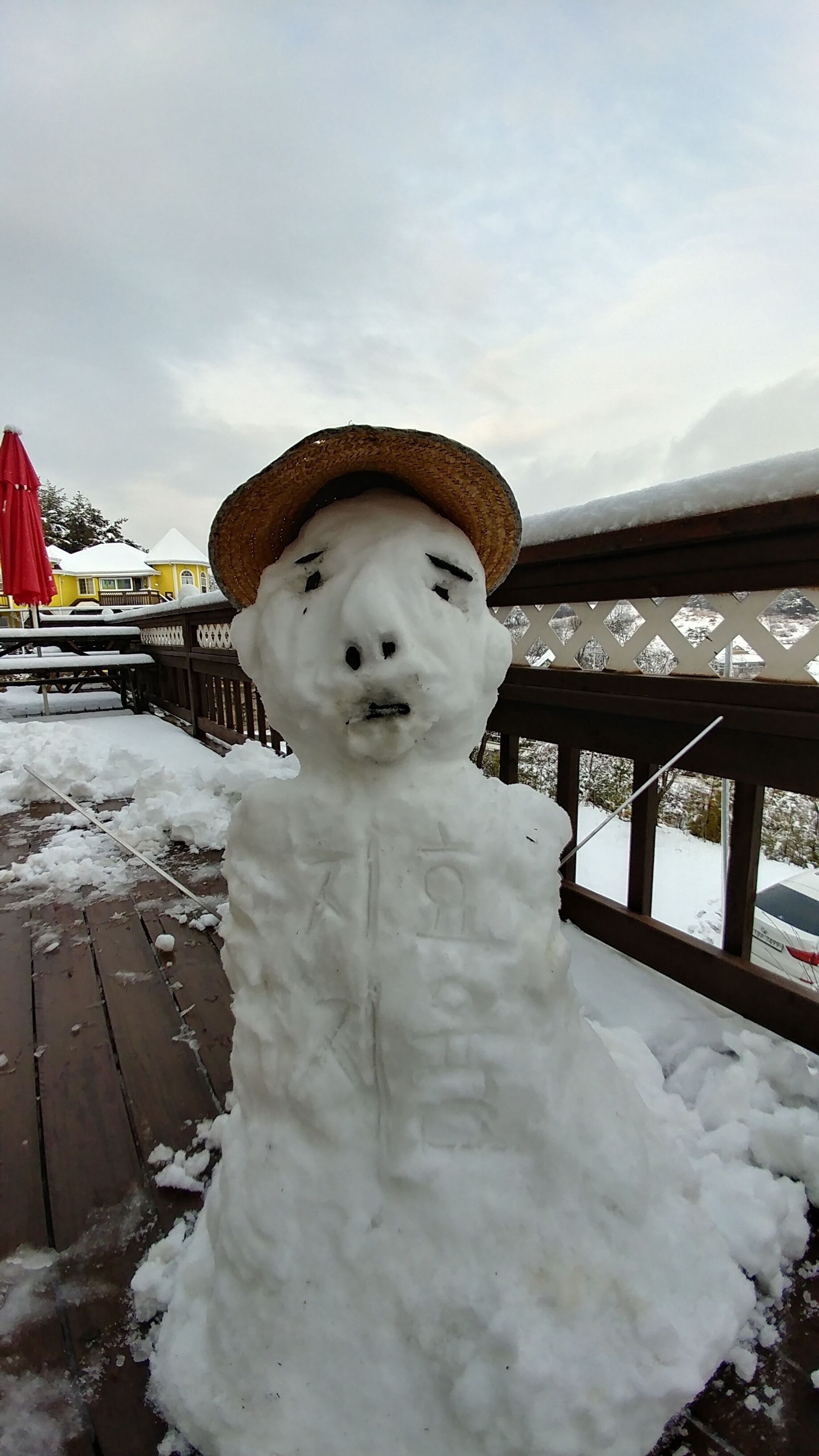 A snowman with a straw hat on a wooden deck.