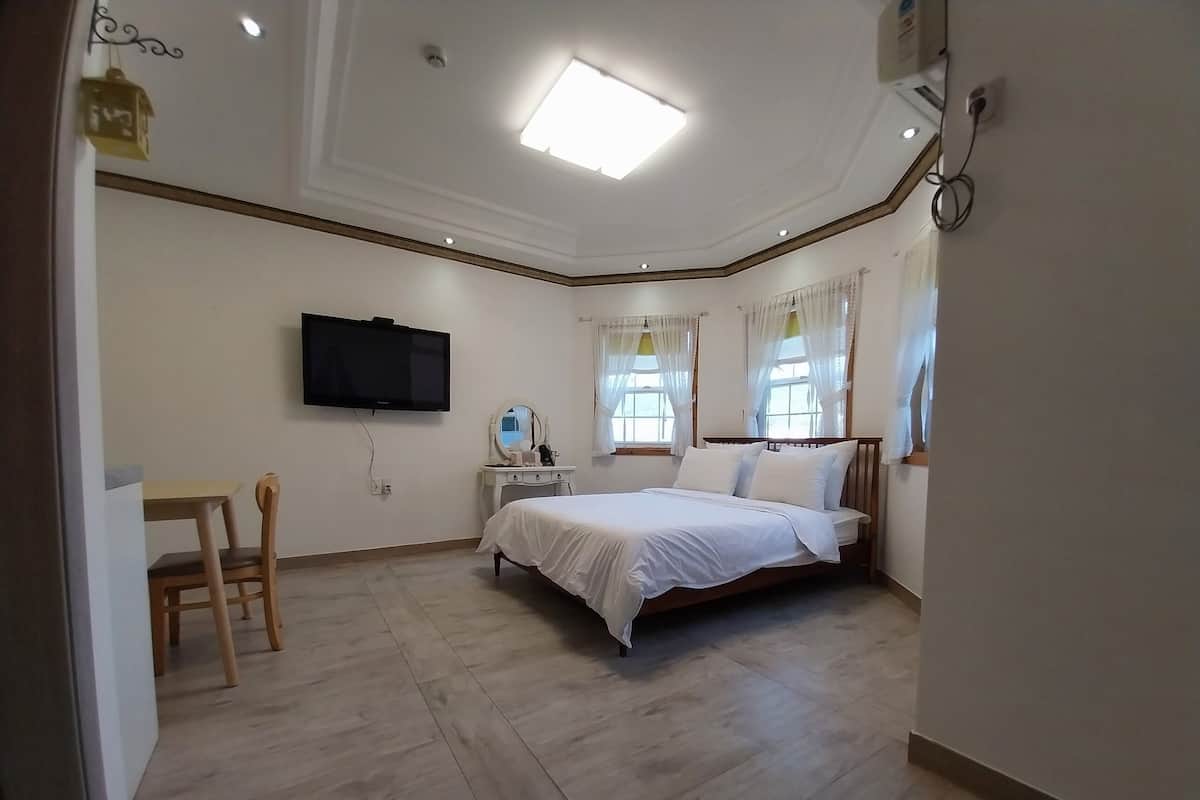 Un dormitorio con cama, televisor montado en la pared, mesita de noche y una silla.