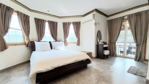 Un dormitorio amplio con una cama grande, un tocador con espejo y varias ventanas con cortinas.