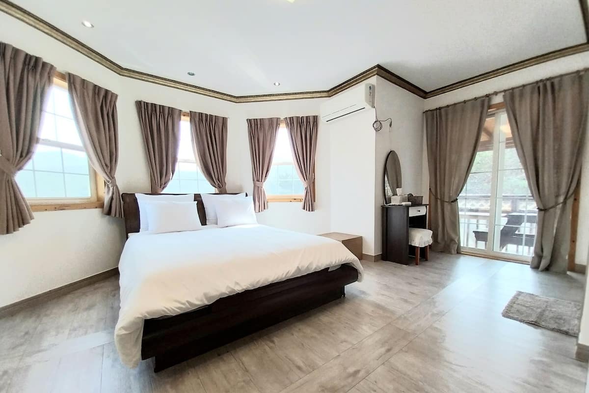 Un dormitorio amplio con una cama grande, un tocador con espejo y varias ventanas con cortinas.