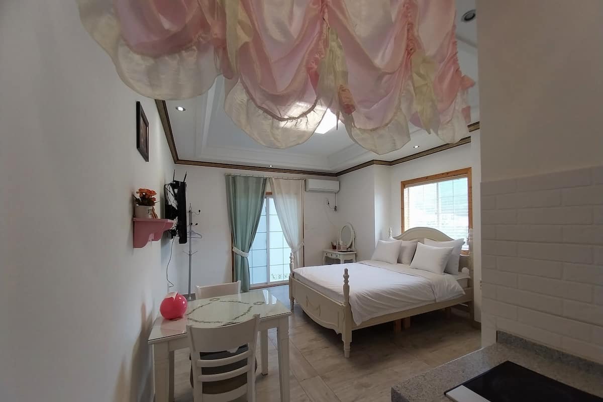 Un dormitorio con cama, una mesita de noche, una silla, una ventana con cortinas y un techo decorado con tela.