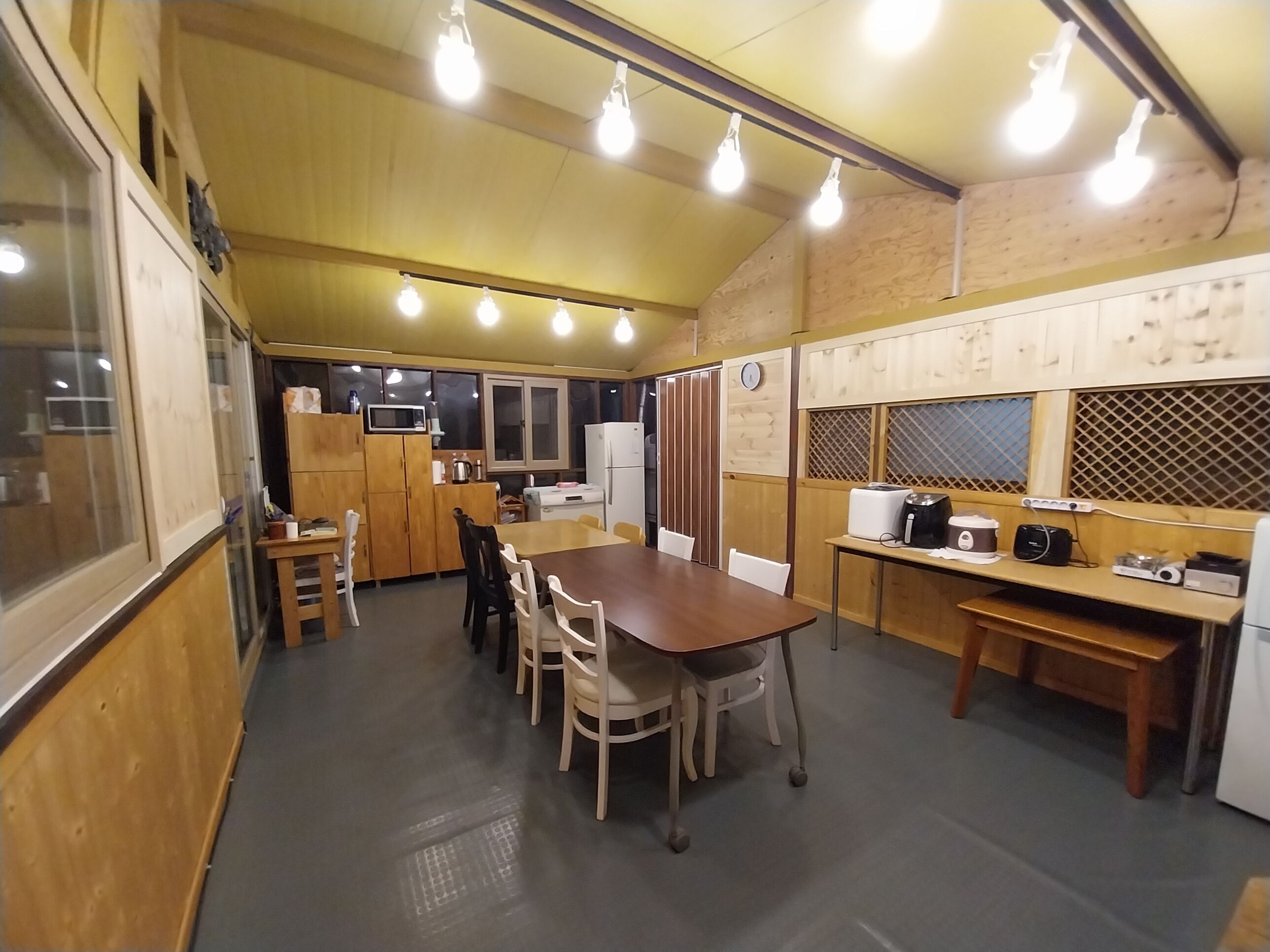 A compact kitchen with wooden cabinets, a dining table, and chairs. There are built-in appliances, including a microwave and a refrigerator.
