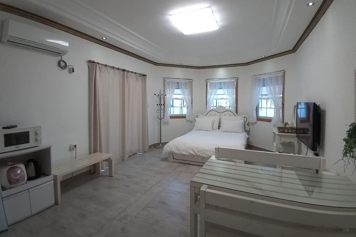 Un dormitorio con cama, televisor, escritorio y perchero.