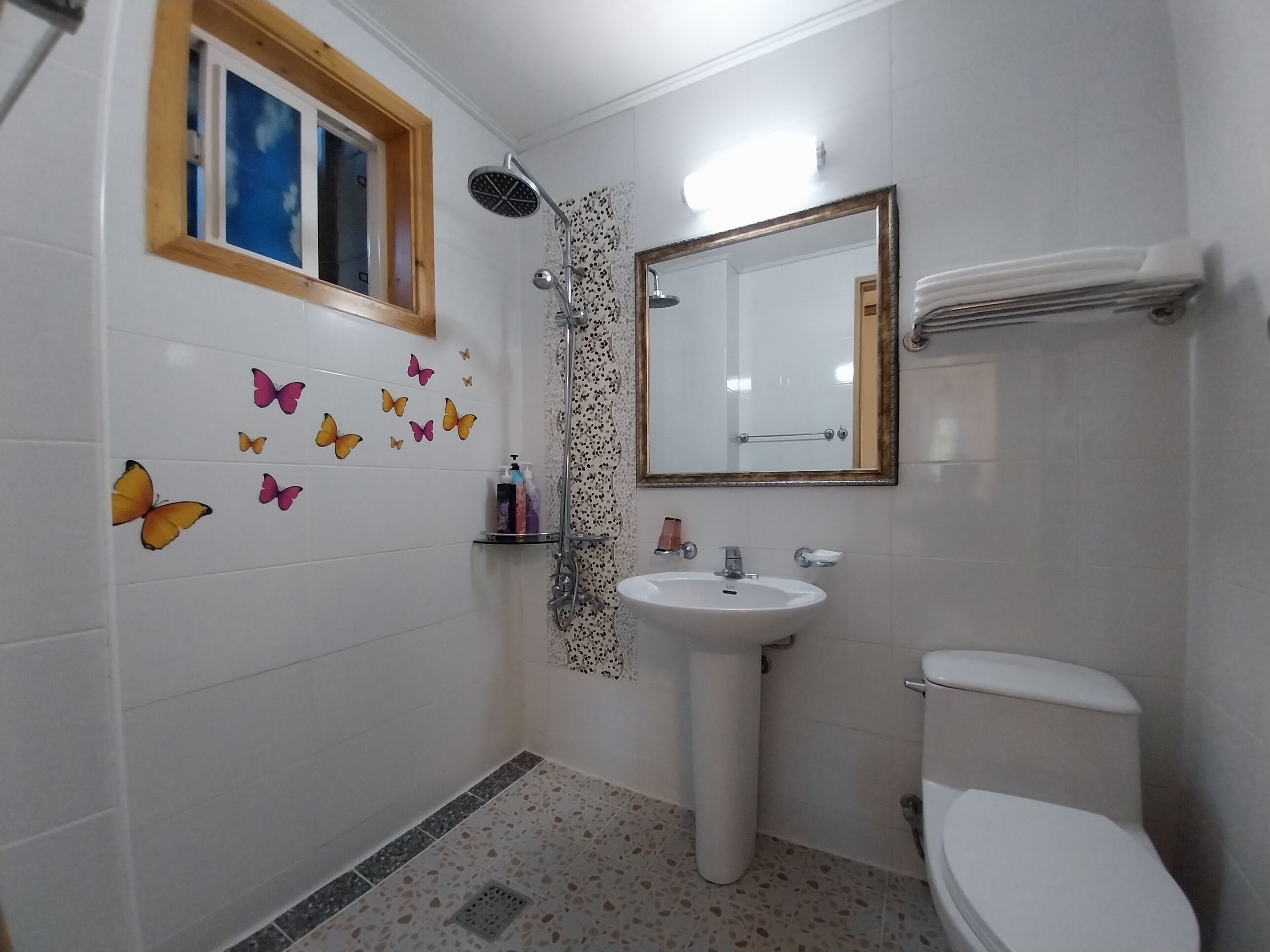 Casa de banho com janela, chuveiro, lavatório e sanita.