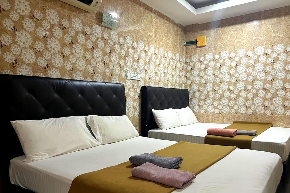 Habitación de hotel con dos camas, cada una con cabecero negro y ropa de cama blanca. Hay toallas sobre las camas y el papel tapiz de las paredes presenta un diseño floral.