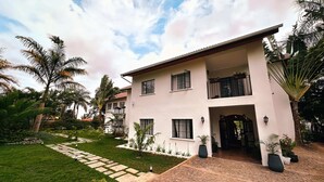 A two-story building with a paved driveway, a well-maintained lawn, and palm trees. - Brubru Lodge  (Moshi)