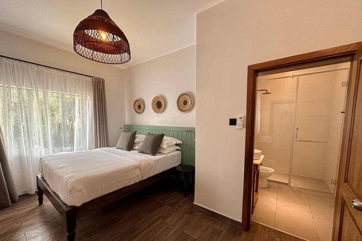 A bedroom with a wooden bed, a hanging light fixture, and a door leading to a bathroom.