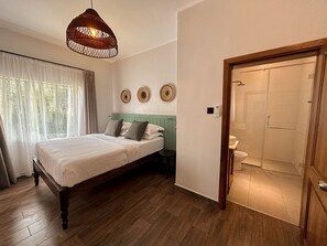 A bedroom with a wooden bed, a hanging light fixture, and a door leading to a bathroom.
