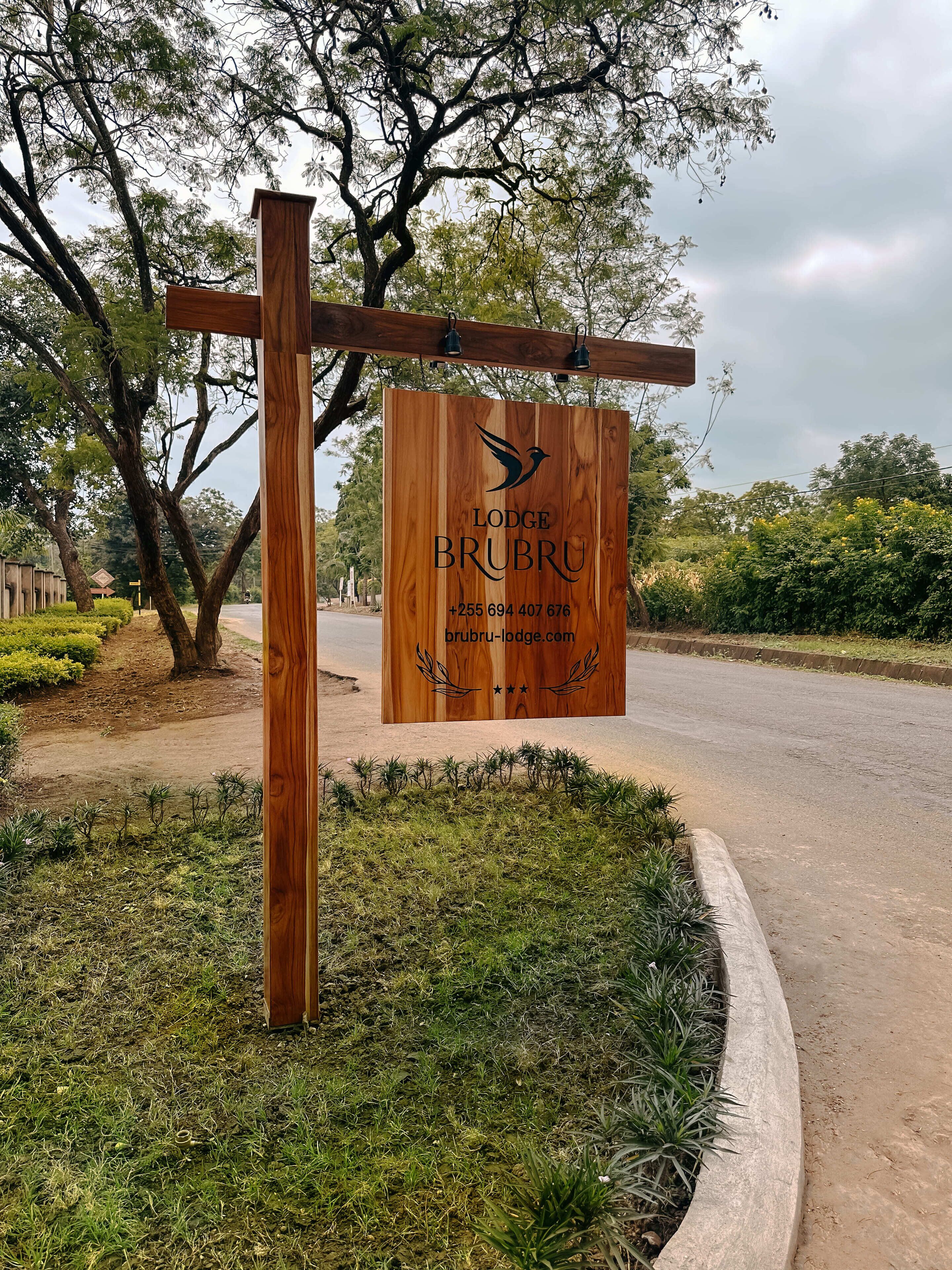 Un letrero de madera del Brubru Lodge con datos de contacto y una dirección web.