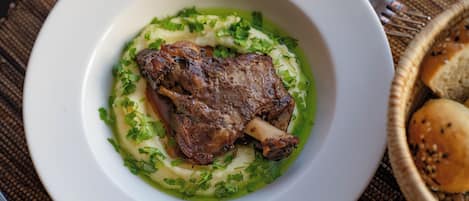 Un piatto con un secondo a base di carne, guarnito con erbe aromatiche, su un piatto bianco.