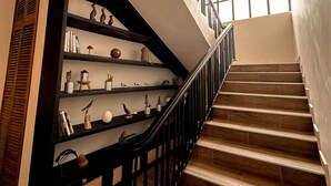 A staircase with wooden steps and black railings, leading to a landing with a black bookshelf and decorative items. - Brubru Lodge  (Moshi)