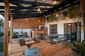 An outdoor dining area with wooden flooring, metal chairs, and hanging pendant lights.