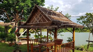 A wooden gazebo with a thatched roof, surrounded by potted plants and a view of a lake. - Changthai Comfort Guest House (Udon Thani)