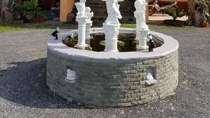 A building with a tiled roof, a central fountain with statues, and a stone pathway leading to the entrance. - Changthai Comfort Guest House (Udon Thani)
