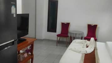 A hotel room with a bed, a desk, two chairs, a refrigerator, and a ceiling fan.