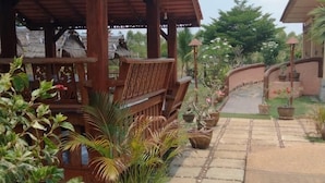 A covered wooden structure with a bench, potted plants, and a paved pathway leading to a building. - Changthai Comfort Guest House (Udon Thani)