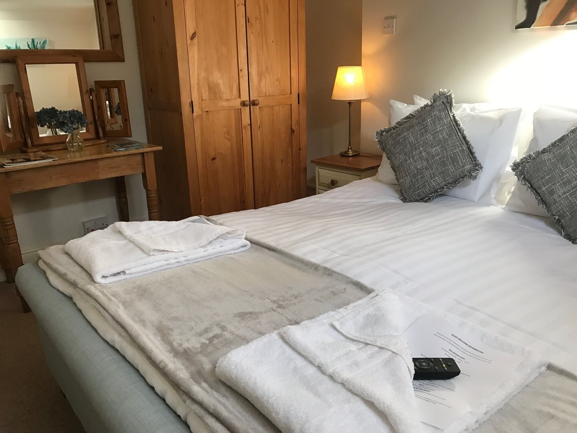 Ein ordentlich bezogenes Bett mit weißen Leinen und Handtüchern, eine Nachttischlampe und ein Holzschrank.