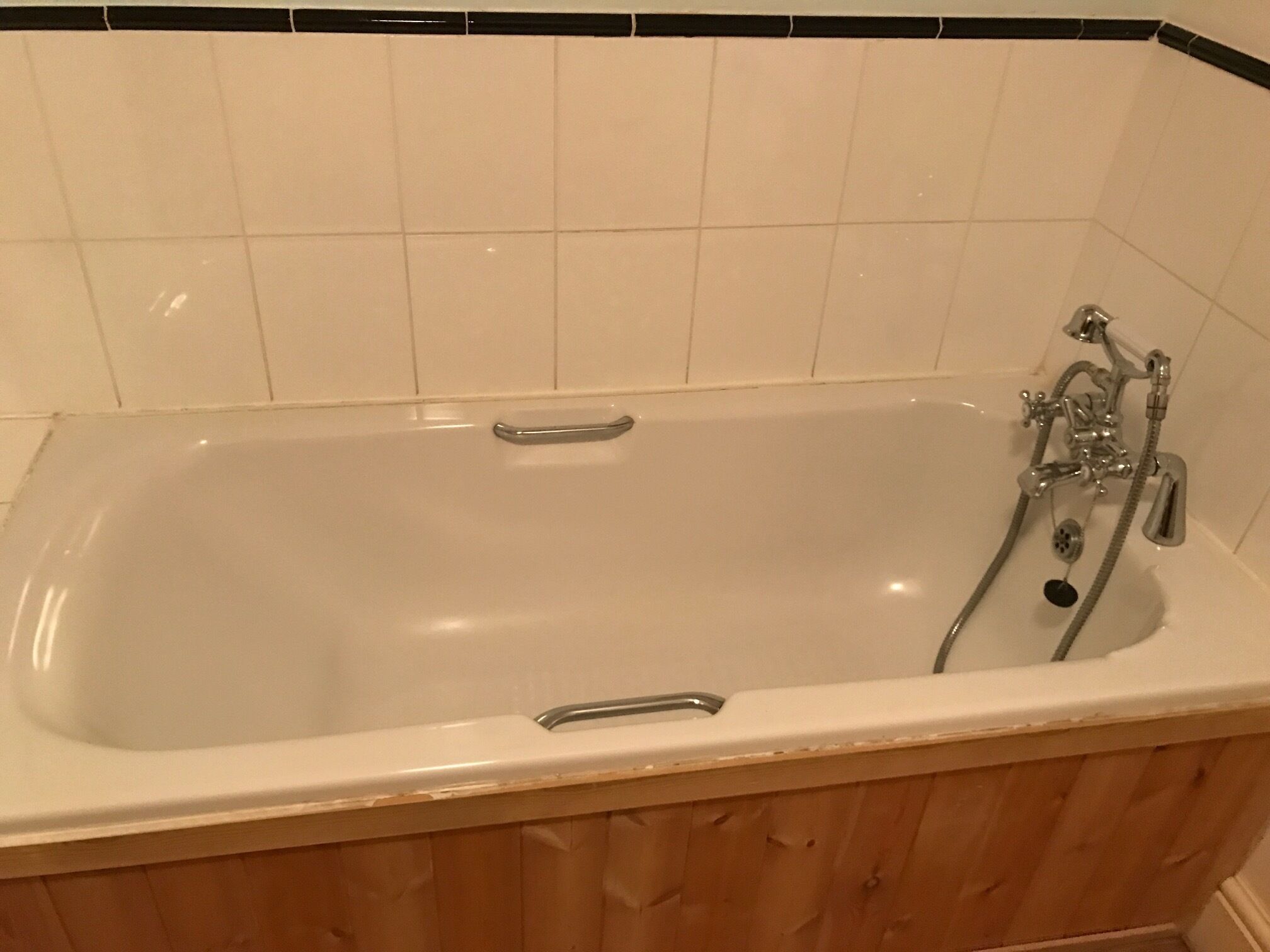 Una bañera blanca estándar con una base de madera y un grifo de cromo.