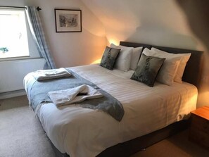 A neatly made bed with a gray and white duvet, a gray throw blanket, and a white towel folded on top. There are three pillows with a rabbit design. A framed picture hangs on the wall above the bed. - The Coach House Inn (Oakham)