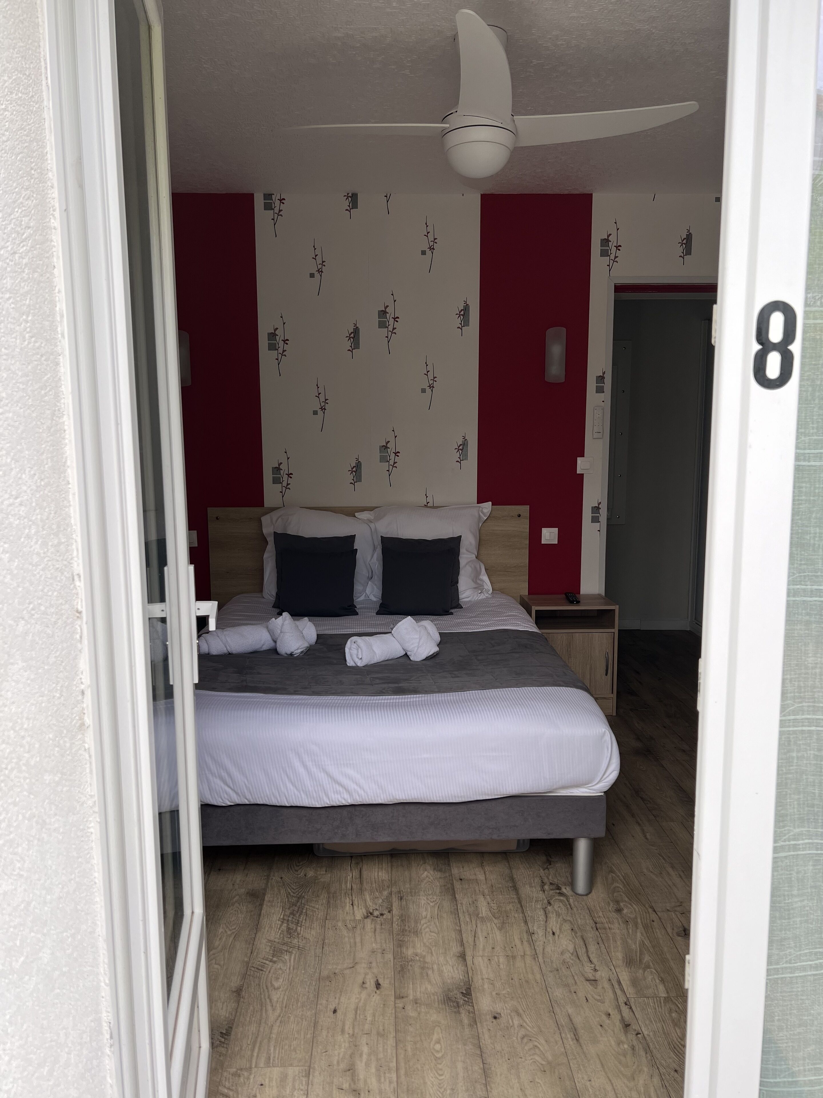 Un dormitorio con una cama, ventilador de techo, mesita de noche y pared con estampado floral.