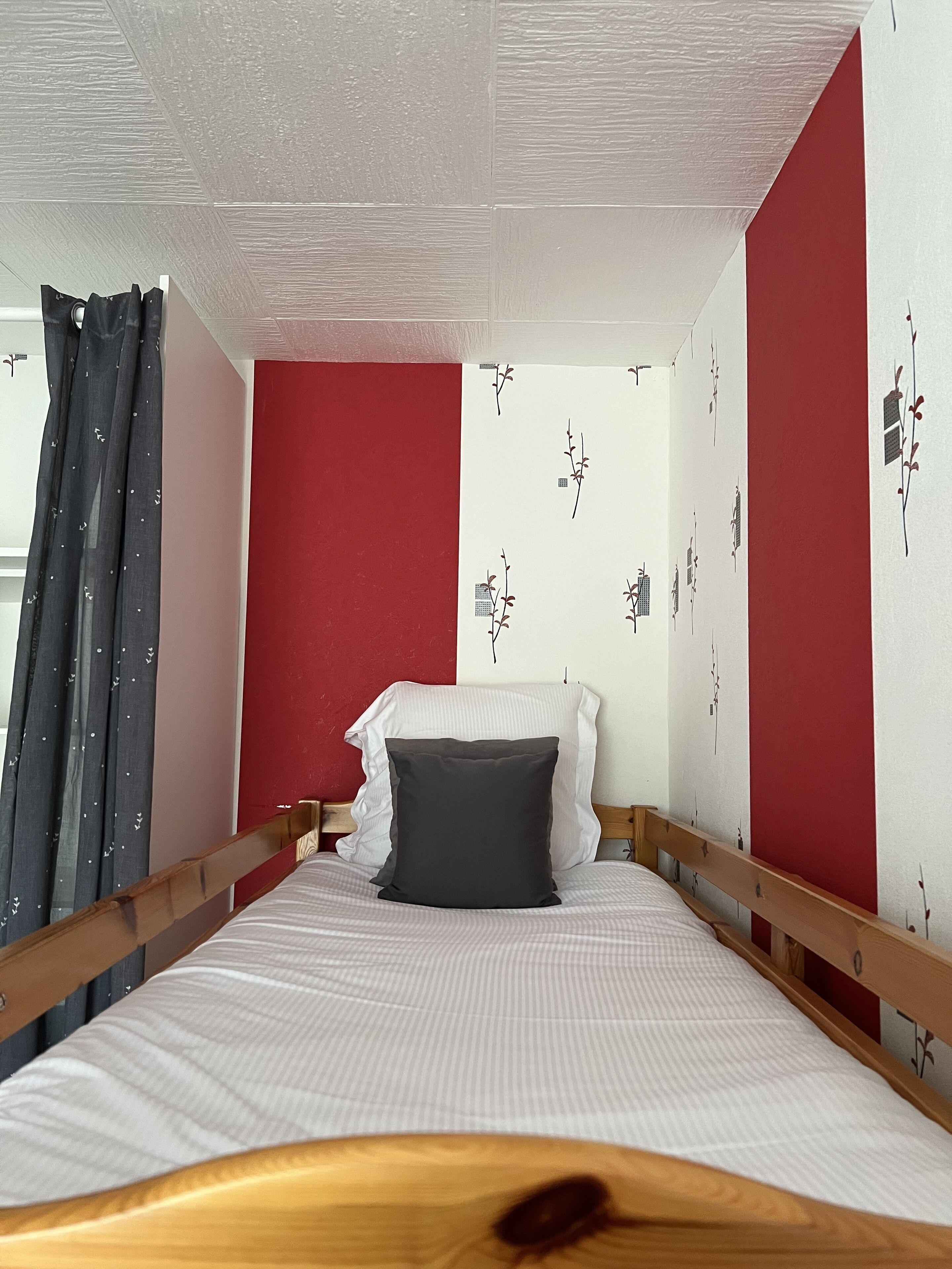 A bedroom with a wooden bed frame, white bedding, red accent walls, and a window with curtains.