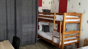 A dormitory room with bunk beds, a desk, a chair, a ceiling fan, and a window with curtains.
