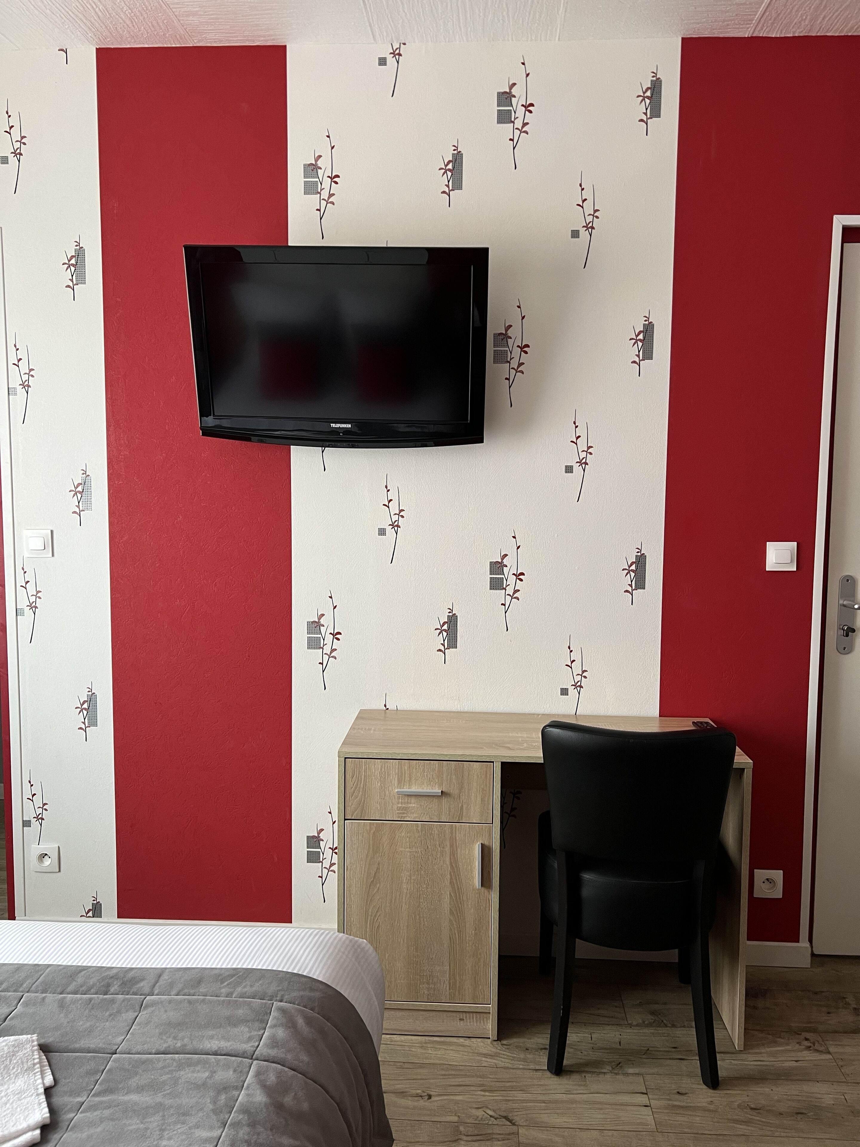 A hotel room with a bed, a desk, a chair, and a TV mounted on the wall.