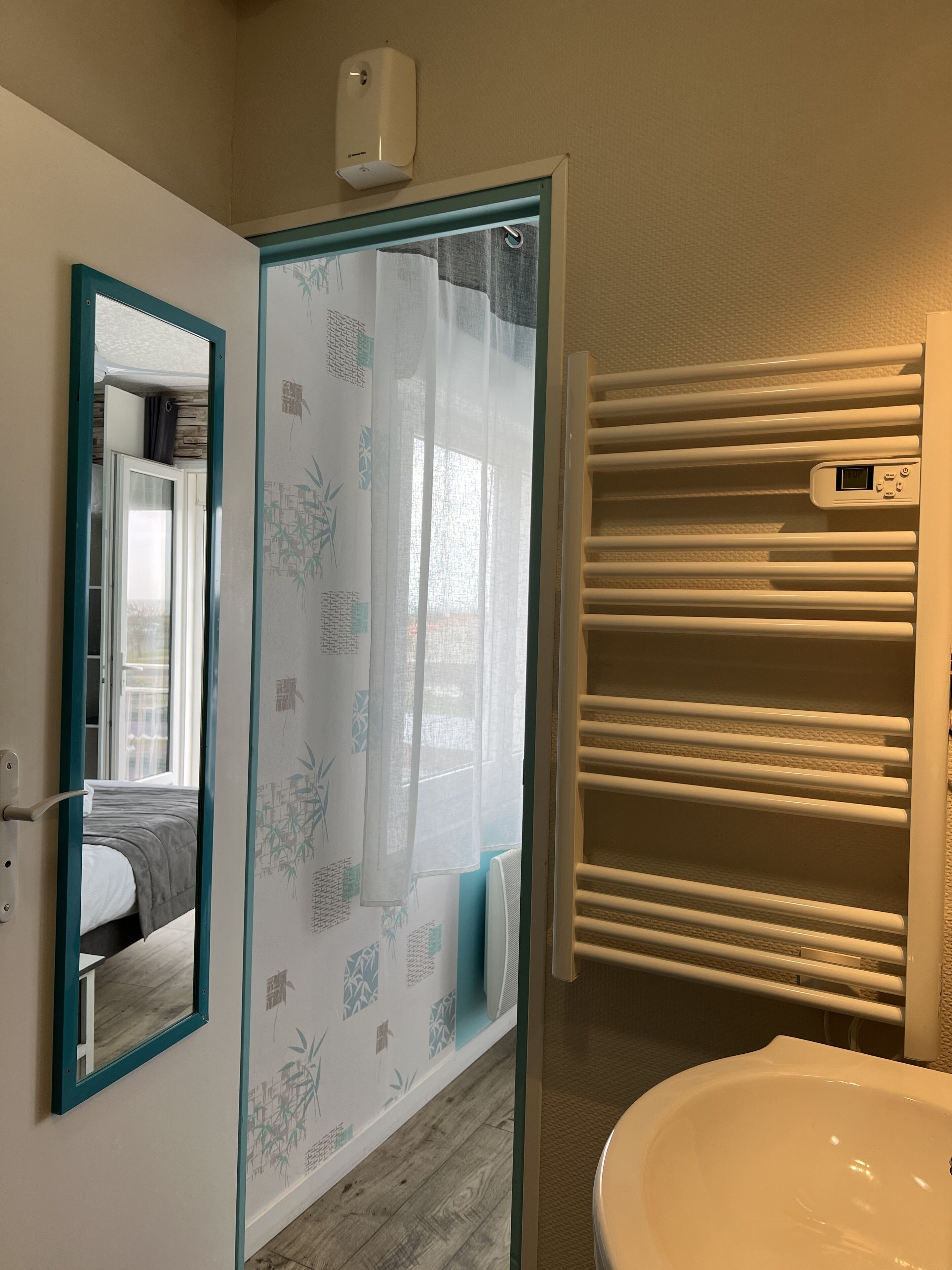 Un baño con puerta de vidrio, espejo, inodoro y toallero.