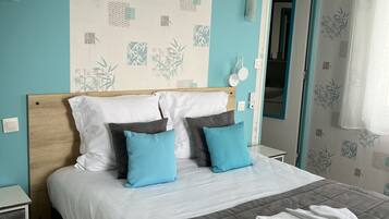 A neatly made bed with a grey quilt, two blue pillows, and a white blanket folded at the foot.