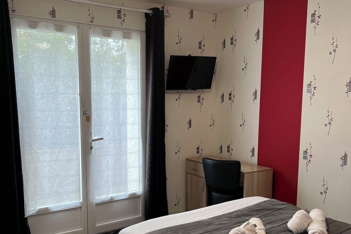 A hotel room with a bed, a desk, a chair, a TV, and a ceiling fan.