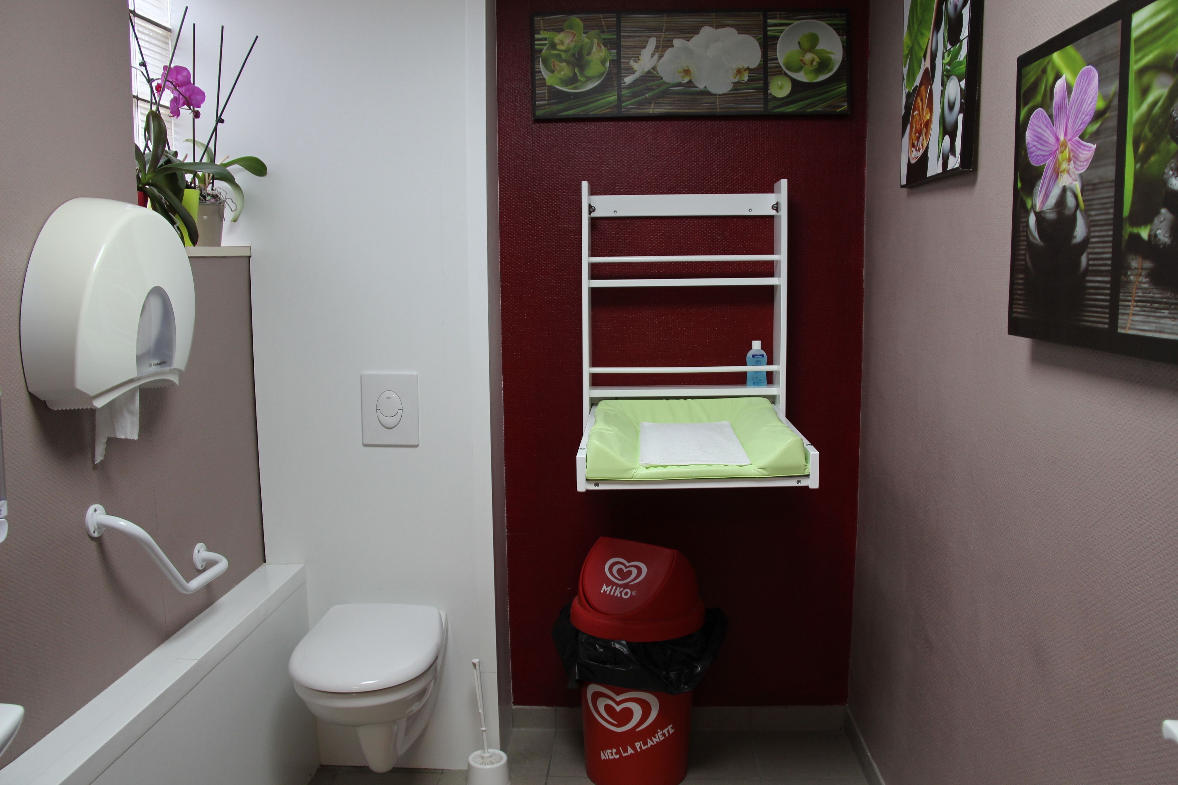 Un baño pequeño con inodoro, secamanos, lavabo, espejo y estante con una planta.