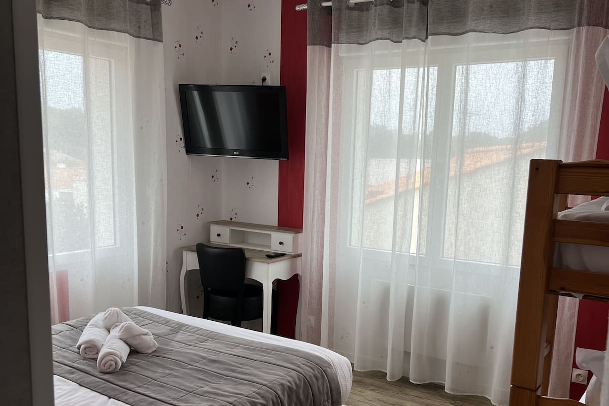 A bedroom with a bed, a desk, a chair, a TV, and a ceiling fan.