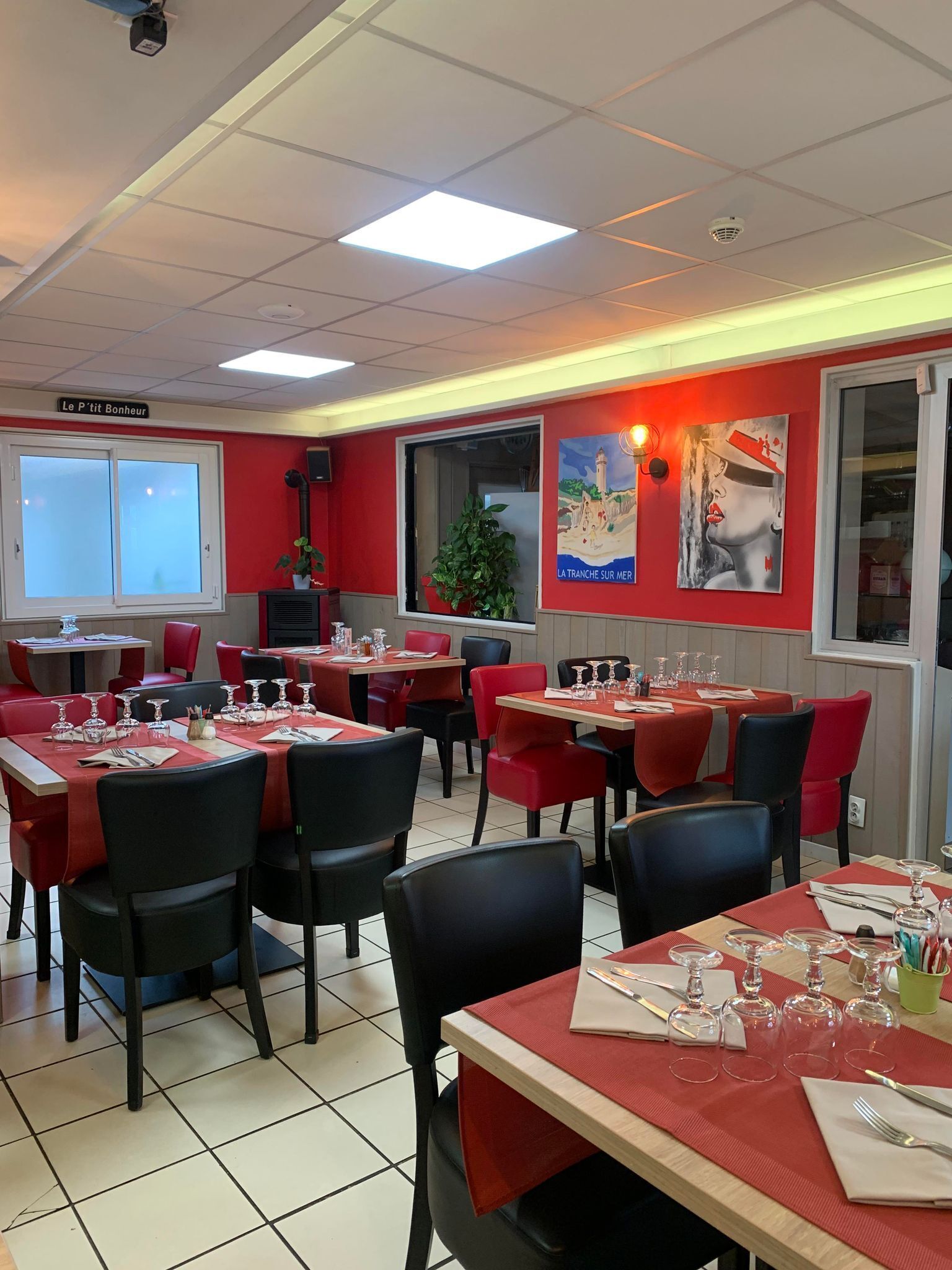 Un restaurant avec des chaises rouges et noires, des tables dressées avec des verres à vin et des couverts, et une grande fenêtre offrant une vue panoramique.