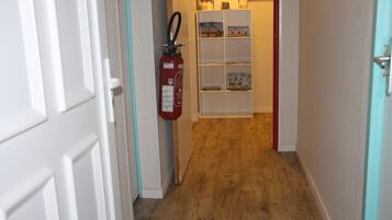 A hallway with a fire extinguisher, a white shelf unit, and a wooden floor.