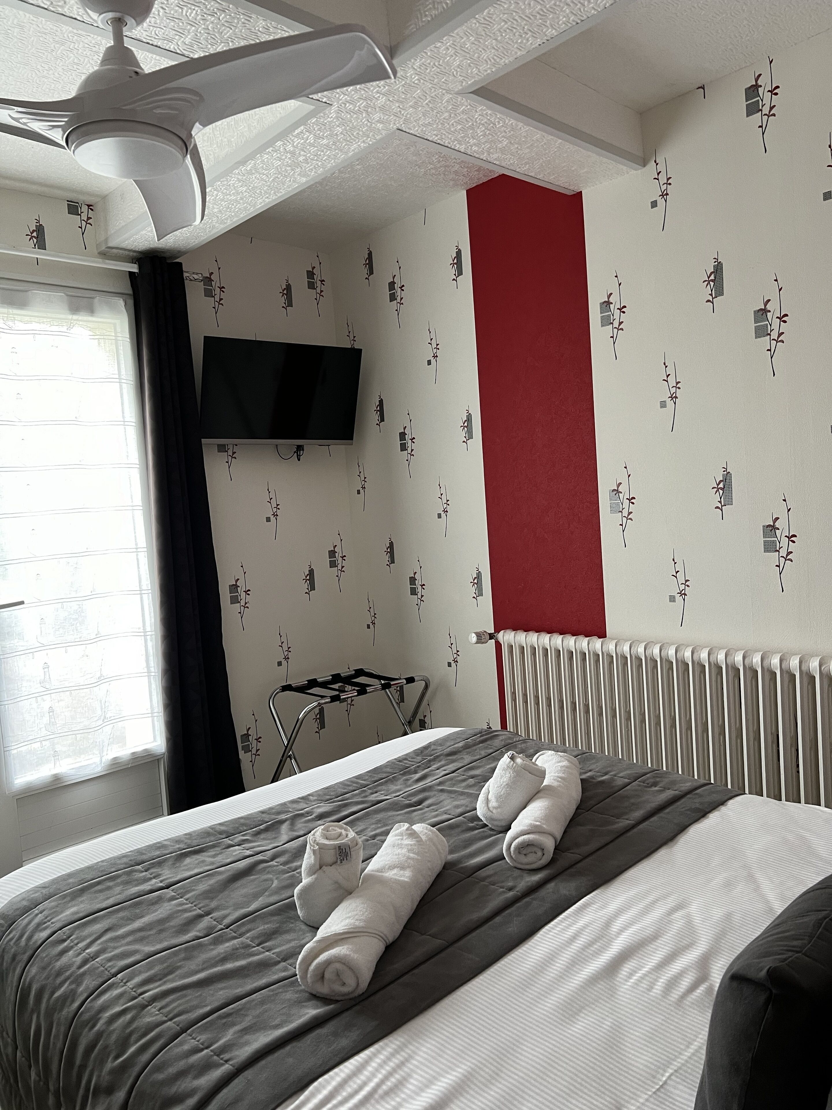 Una habitación de hotel con cama, ventilador de techo, televisor montado en la pared y radiador.