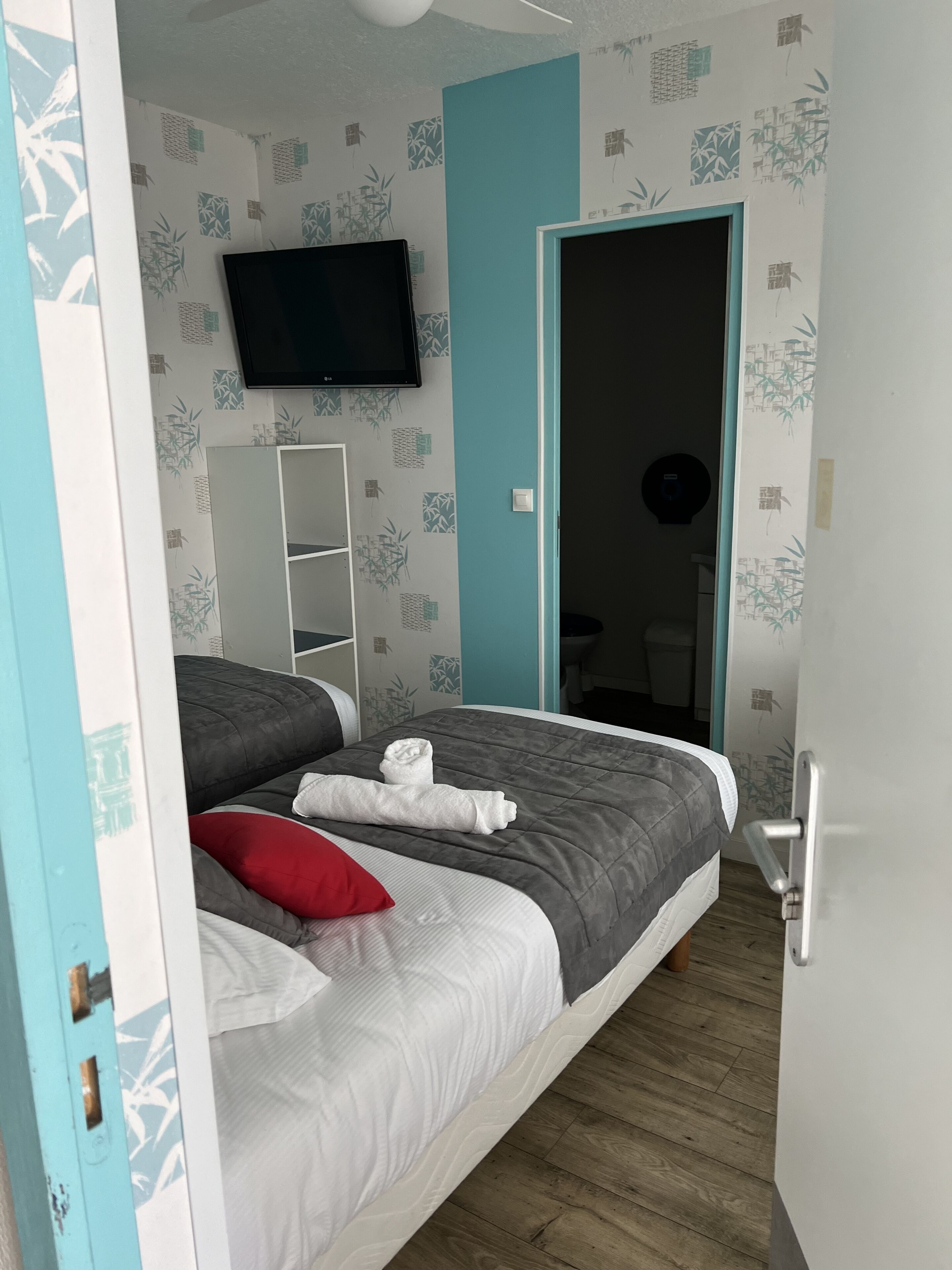 Un dormitorio con cama, televisor y puerta que da a otra habitación.