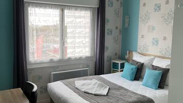 A bedroom with a bed, a desk, a chair, a ceiling fan, and a window with curtains.