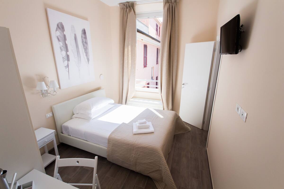 Habitación de hotel con cama, escritorio, silla, televisor y ventana con cortinas.