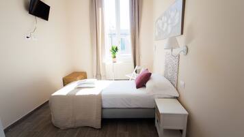 Ein Schlafzimmer mit Bett, Nachttisch, Lampe, Fernseher, Fenster und einer Zimmerpflanze.