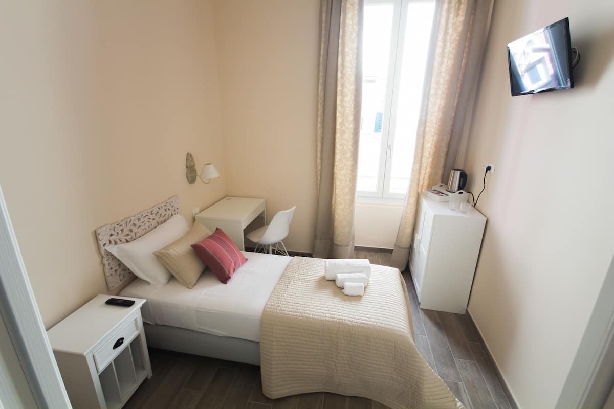 Habitación de hotel con cama, mesita de noche, silla, escritorio, televisión y un mueble bajo.
