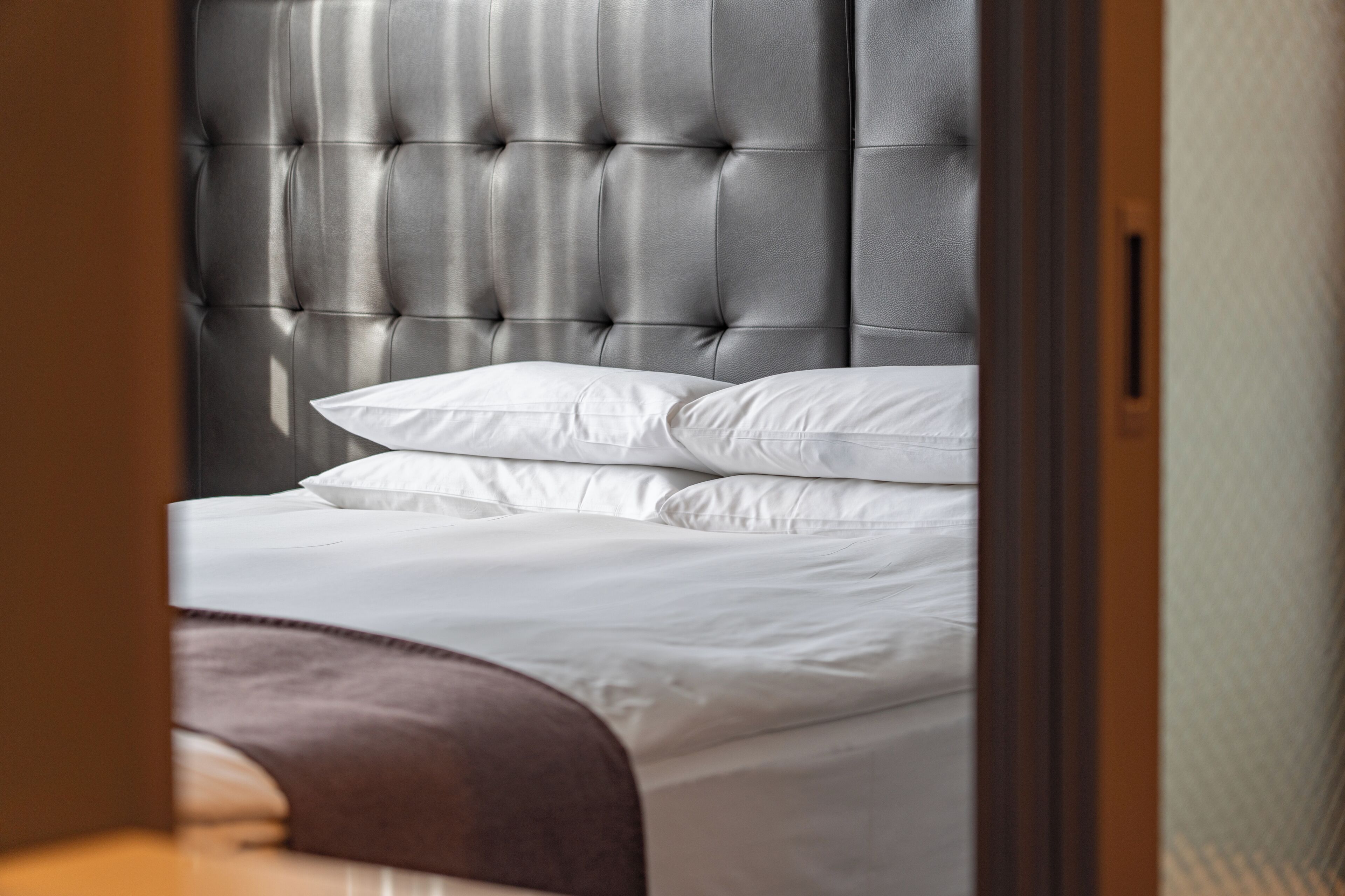 A neatly made bed with white linens and a tufted headboard.