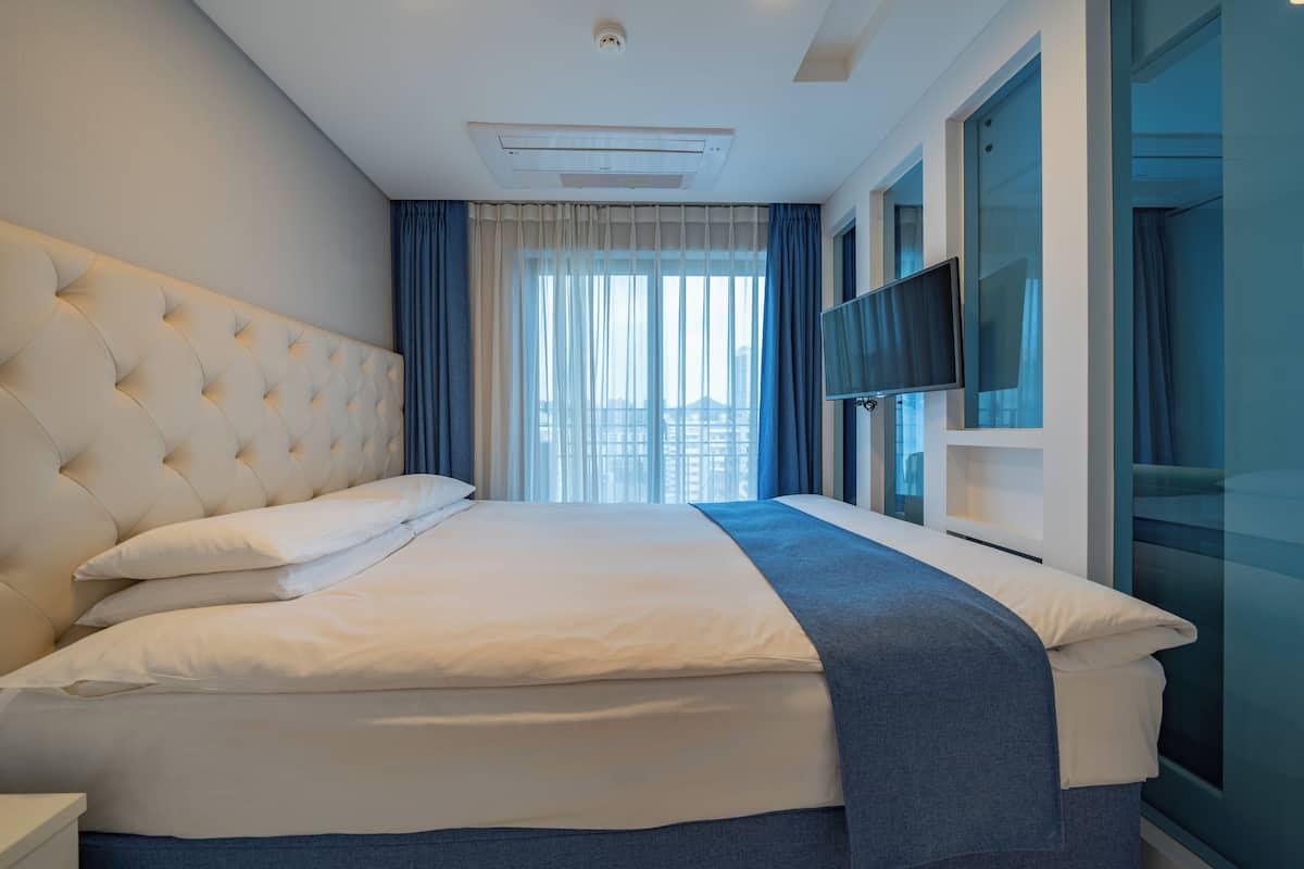 Quarto de hotel moderno com uma cama grande, televisão de tela plana e vista da cidade pela janela.