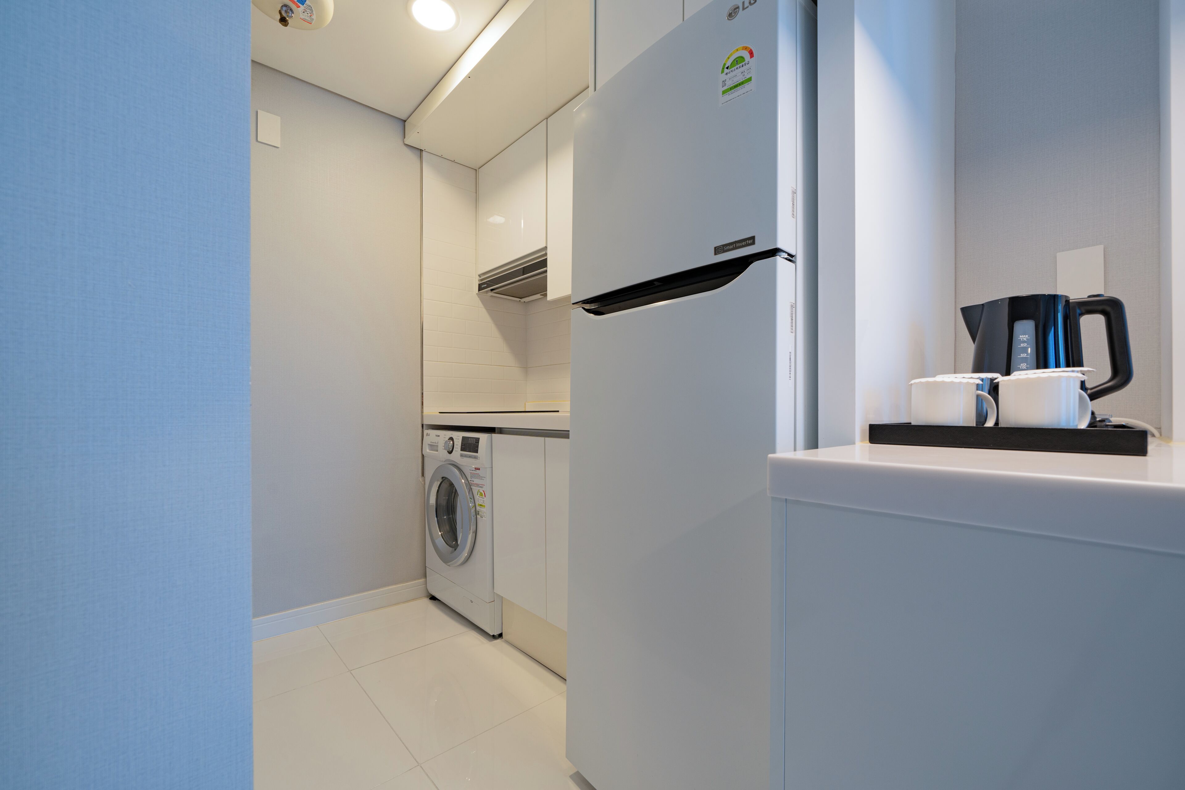 A compact kitchen with a washing machine, a refrigerator, and a coffee maker.