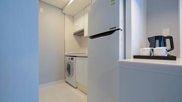 A compact kitchen with a washing machine, a refrigerator, and a coffee maker.