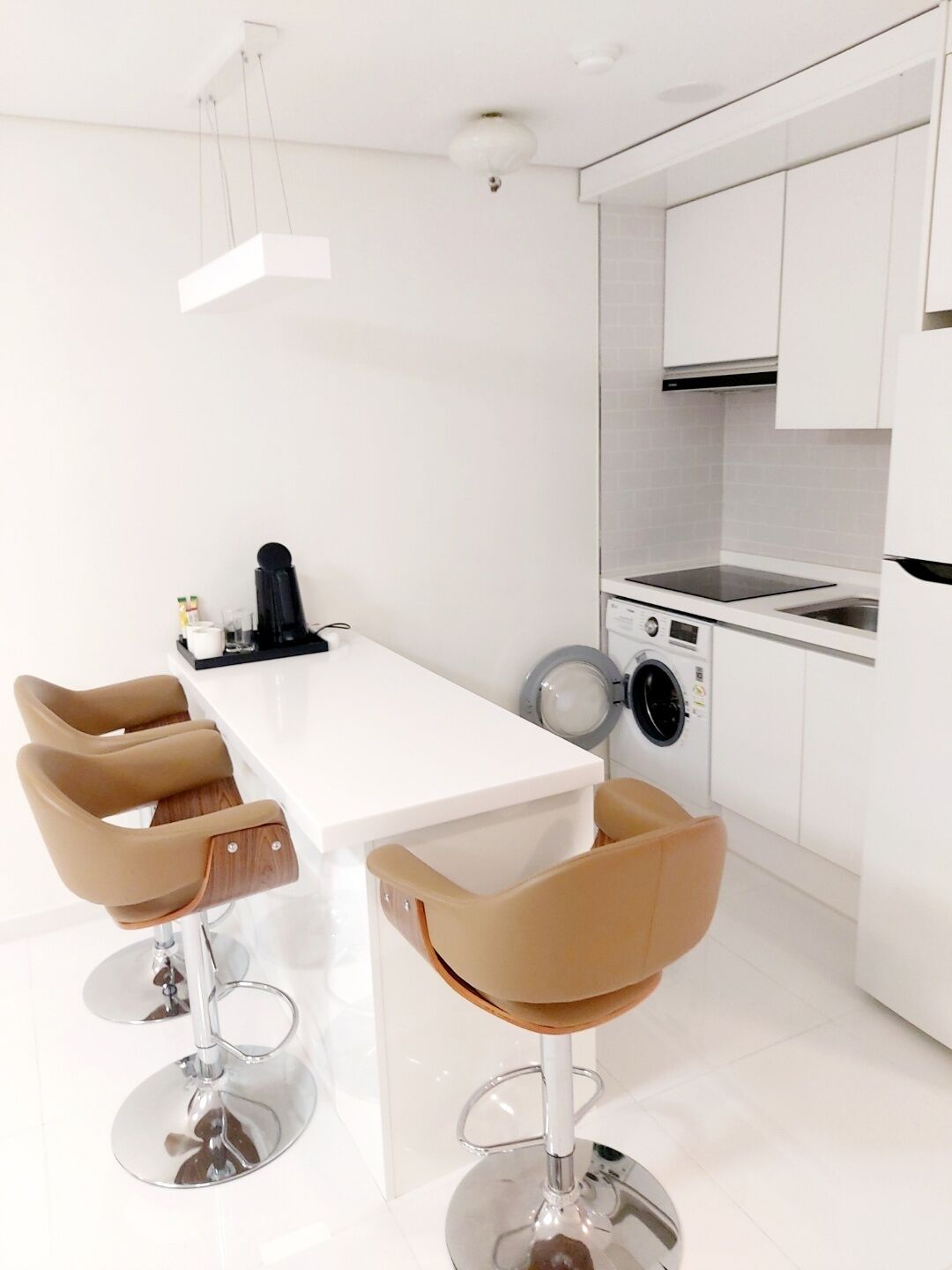 Una cucina moderna con mobili bianchi, un'isola centrale con sgabelli da bar, una lavatrice e una macchina da caffè.