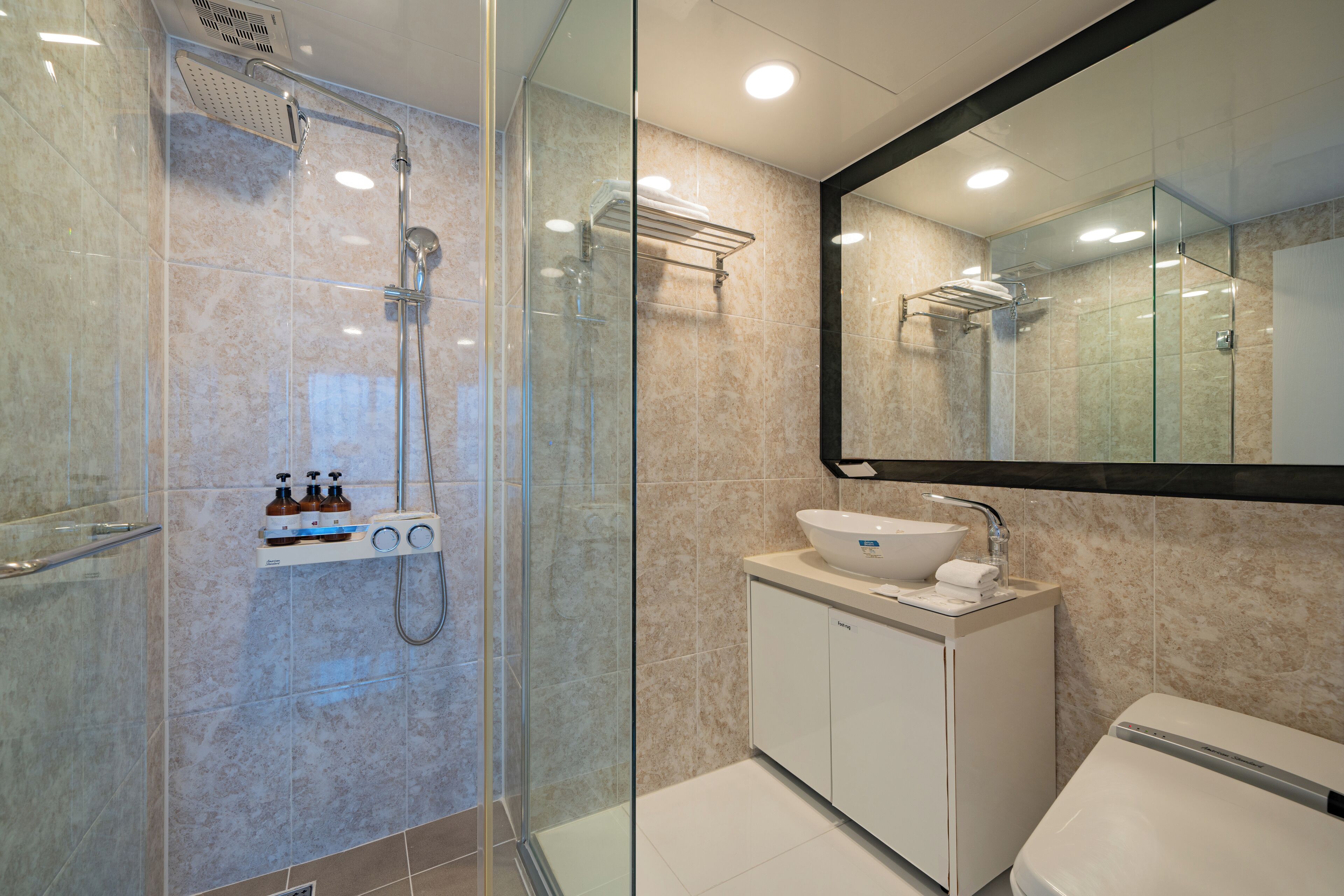 Un baño moderno con ducha de vidrio, lavamanos blanco y un espejo grande sobre el lavamanos.