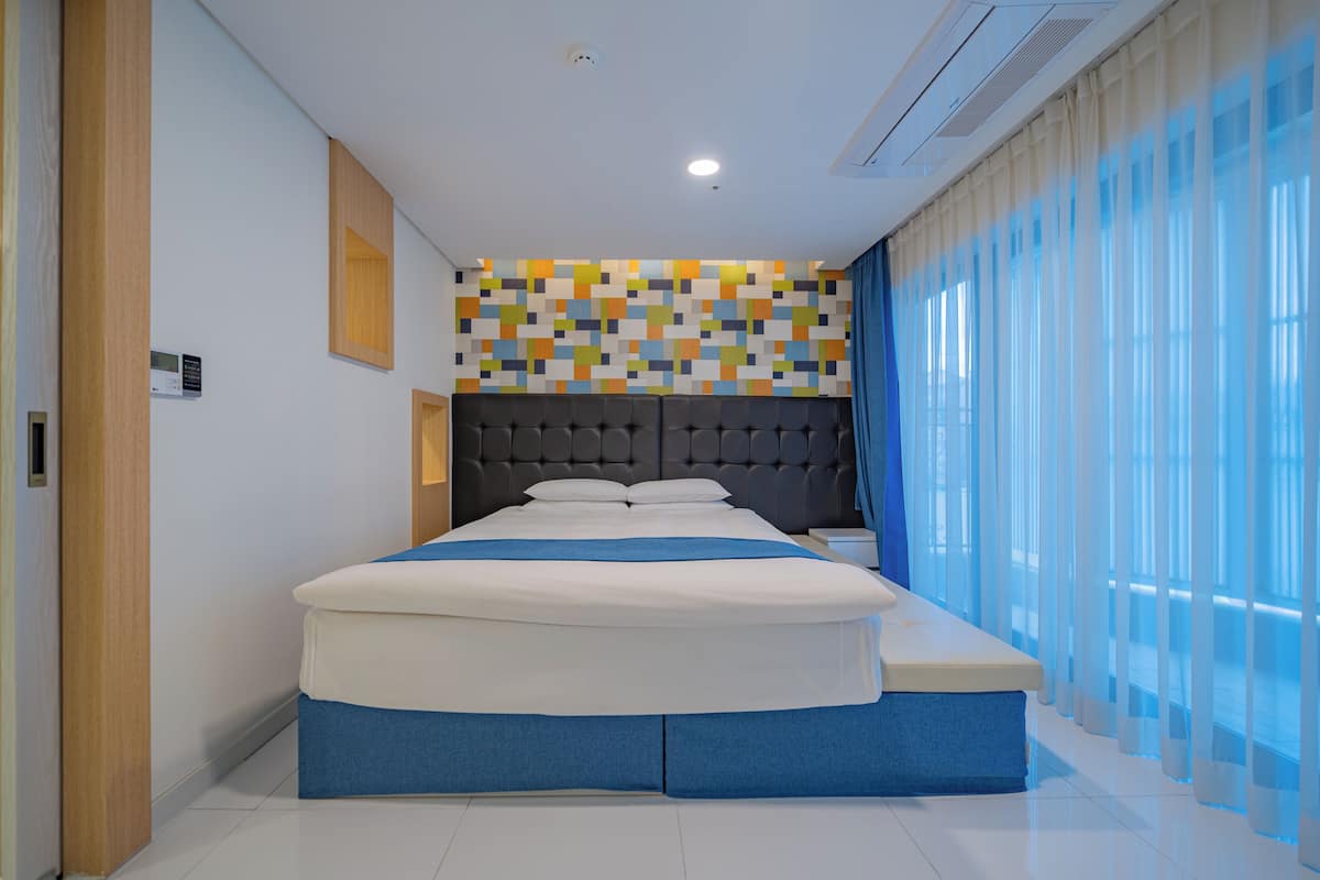 Quarto moderno com uma cama grande, cabeceira estofada e parede com mosaico colorido.
